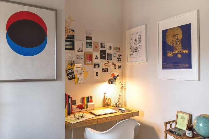 Home office with a wooden desk, white chair, desk lamp, wall art, and a collage of photos and notes.