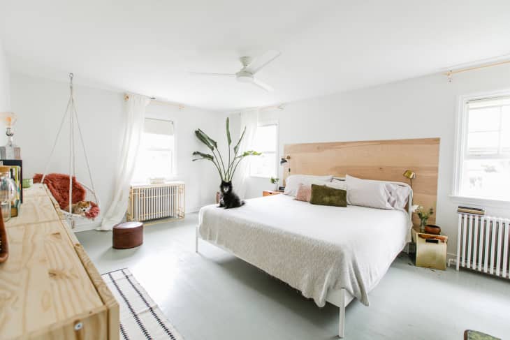 Bright bedroom with a large bed, wooden headboard, hanging chair, plants, and a cat sitting on the bed.