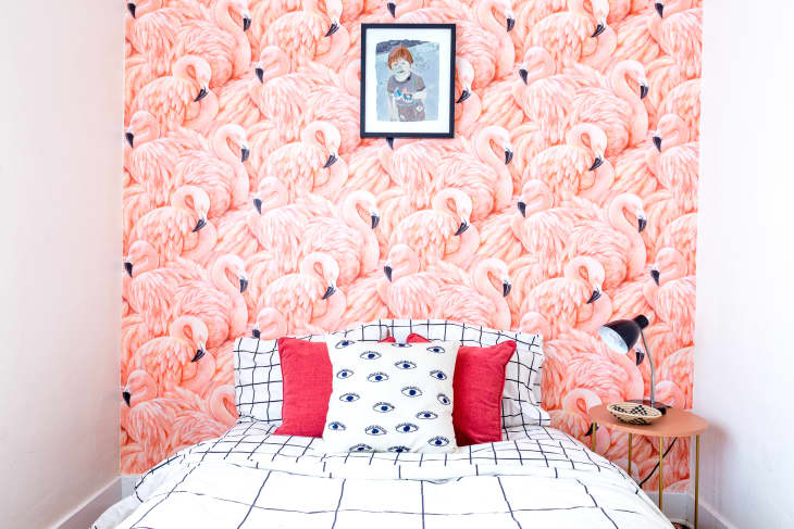 A single bed with mattress, covered in checkered bedsheet, sits against a floor-to-ceiling photo of swans