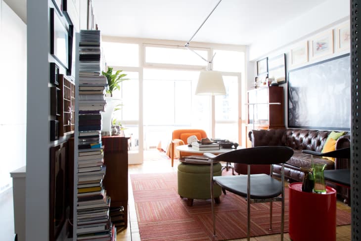 Living room with a brown leather sofa, bookshelves, orange armchair, and a large window.