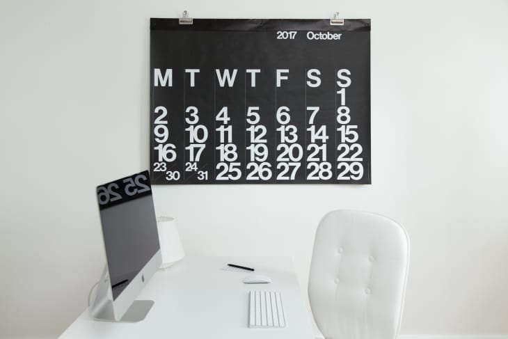 Minimalist office with a large black calendar for October 2017, white desk, iMac, and white chair.