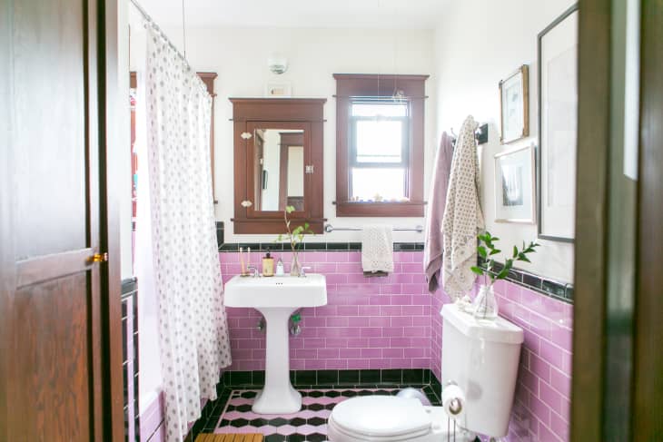 Bathroom with pink subway tiles, pedestal sink, white shower curtain, and framed art on walls.