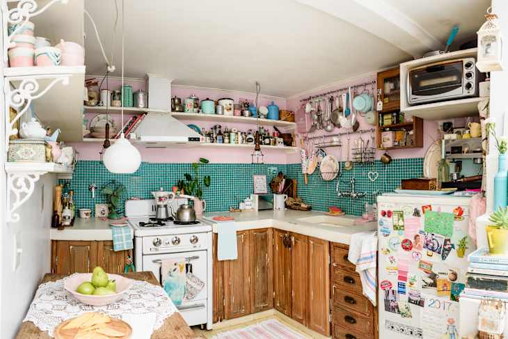 Cozy kitchen with teal tile backsplash, vintage stove, wooden cabinets, and shelves filled with colorful mugs and jars.