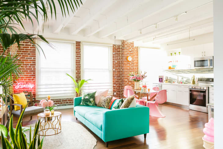 A colorful apartment with an open floorplan, a teal couch, and an exposed brick wall