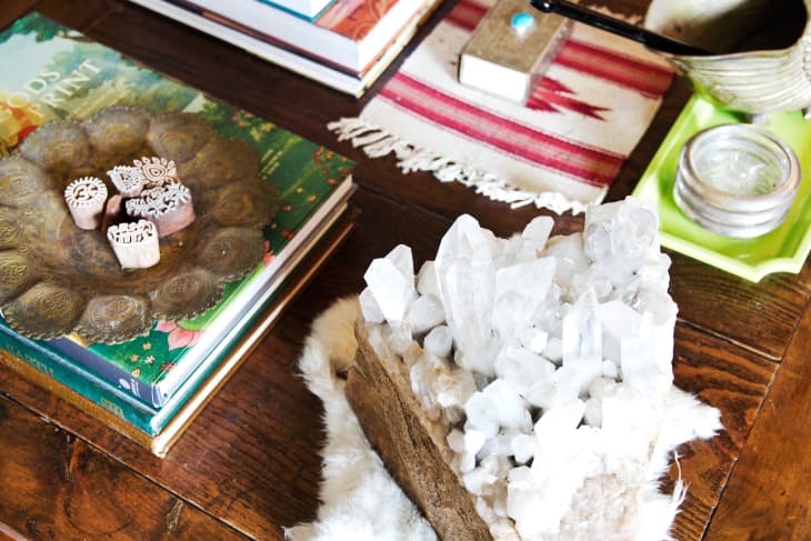 Books and decorative items on a wooden table, featuring a large crystal cluster and a brass tray with carved stamps.