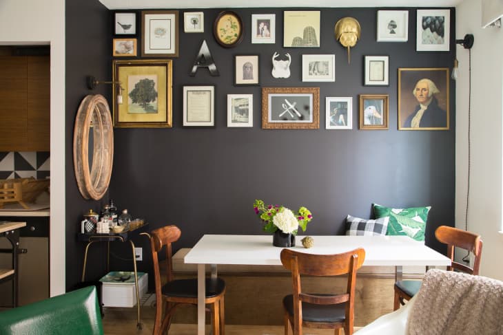 Dining area with a white table, wooden chairs, and a gallery wall of framed art and photos on a dark accent wall.