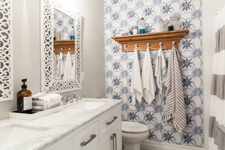 Bathroom with marble countertop, ornate mirror, wooden shelf with hooks, and blue patterned wallpaper.