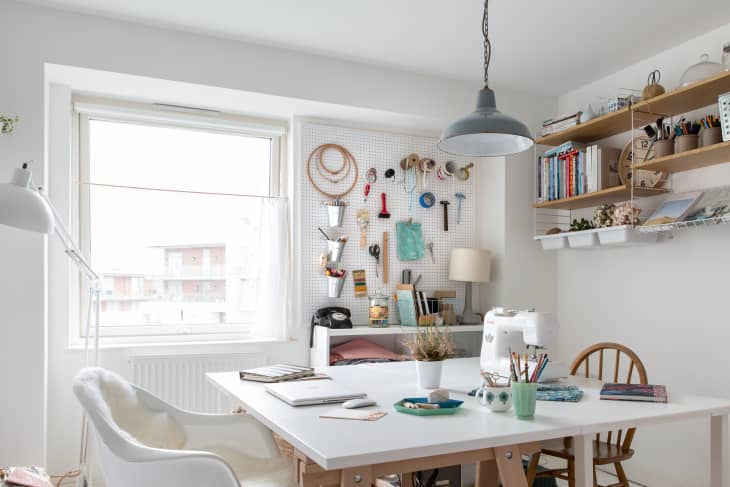 Craft room with a large table, sewing machine, pegboard with tools, shelves with books, and a window with natural light.