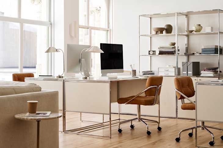 Modern office space featuring two desks with computers, stylish brown chairs, and a metal shelving unit with decor items.