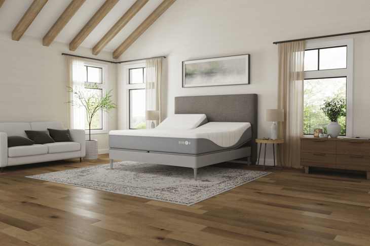 Modern bedroom featuring a gray adjustable mattress, white sofa with dark cushions, and wooden furniture.
