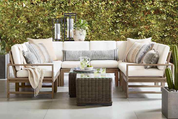 Outdoor seating area featuring a sectional sofa with cream cushions, decorative pillows, and a glass-top coffee table.