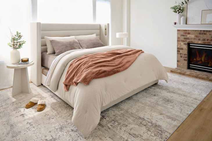 Cozy bedroom featuring a beige bed with a rust-colored throw, a side table, and a fireplace.