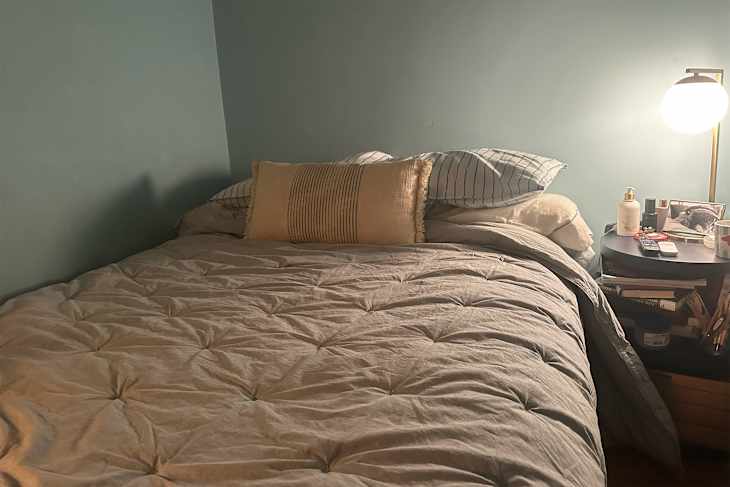 Cozy bedroom with a queen bed, gray comforter, striped pillows, and a bedside table with decor and personal items.