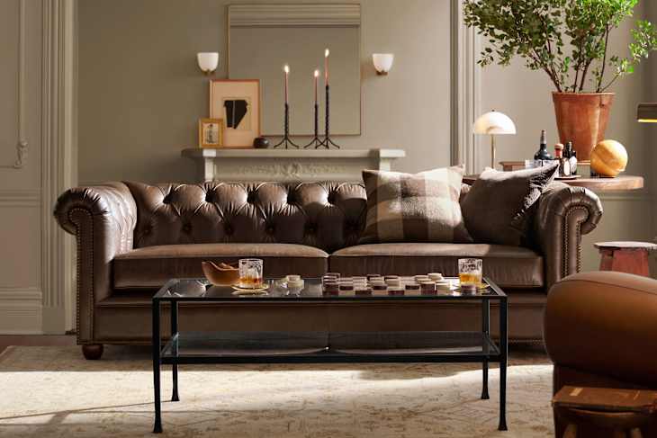Chesterfield sofa with brown leather upholstery, plaid pillows, glass coffee table, and decorative items on a rug.