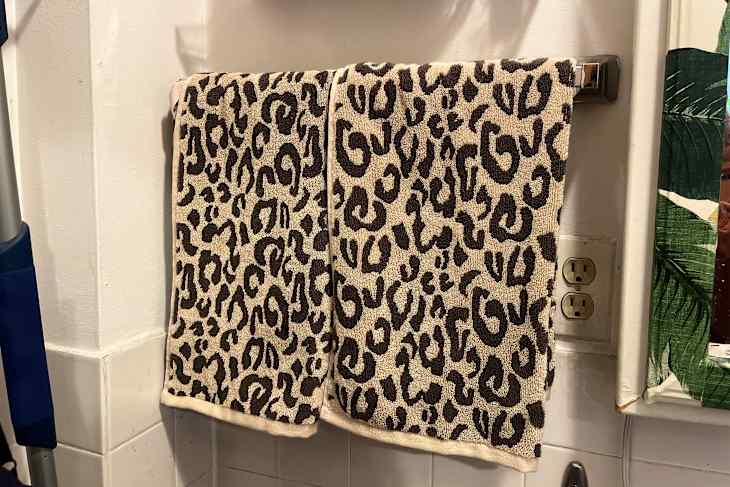 Two leopard print towels hanging on a towel rack in a bathroom, with a white wall and electrical outlets visible.