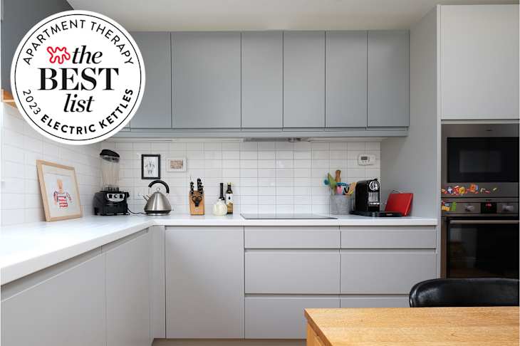 Kitchen with white tile backsplash and grey cabinets. Kitchen appliances line white countertops. The Best List for 2023 Electric Kettles on top left corner.