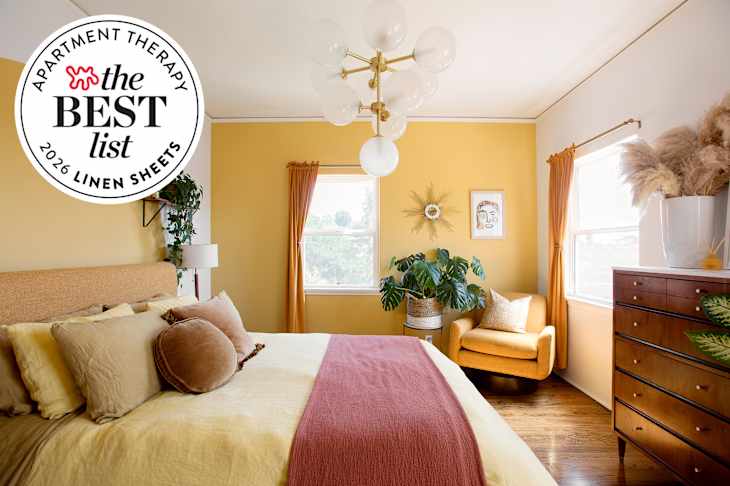 Bright yellow bedroom featuring a bed with layered pillows, a cozy armchair, and a large plant by the window.