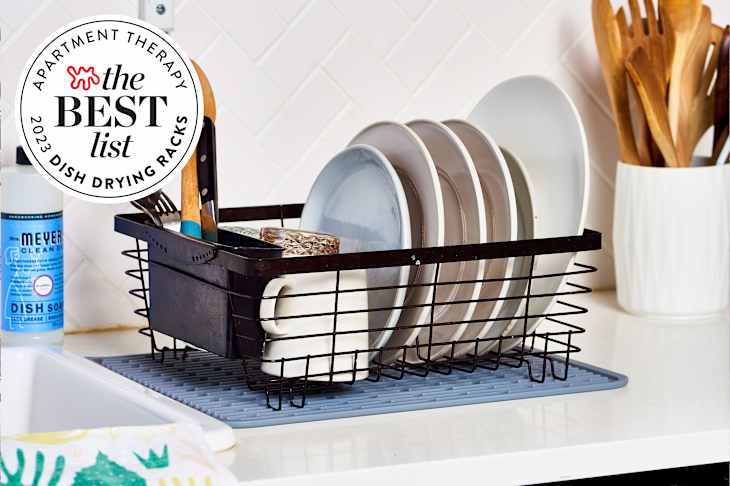 Black dish drying rack full of dishes and utensils sitting on a kitchen counter next to the sink. There is a seal in the upper left corner that reads "Apartment Therapy the Best List 2023 Dish Drying Racks"