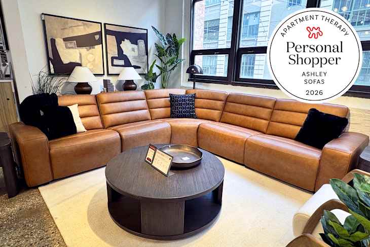 A modern living room featuring a brown leather sectional sofa, round wooden coffee table, and decorative plants.