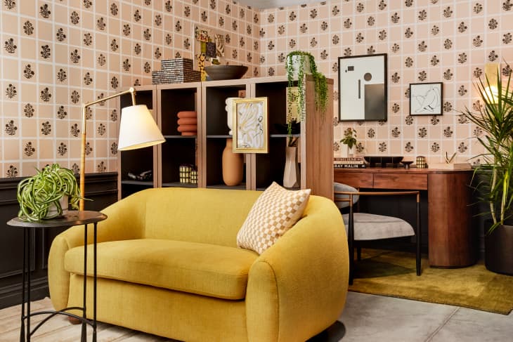 room with DIY wallpaper, gold loveseat, wood desk, shelves with l'objets, plants, gold rug