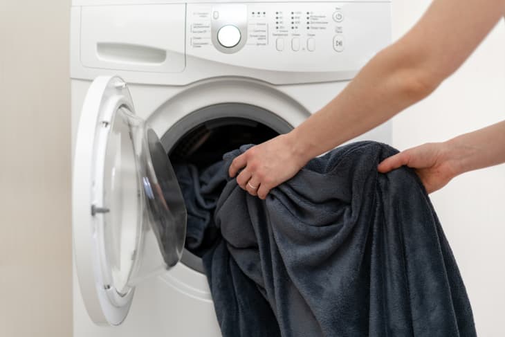 Woman hands put laundry into the white washing machine. She standing inside bright apartment with light interior