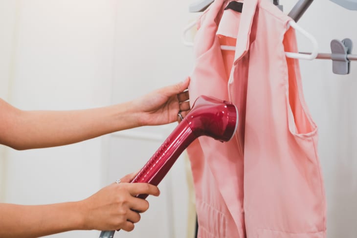 Woman using steaming iron to ironing fashion shirt in laundry room. Girl doing stream vapor iron for press clothes in hand. Launder concentrate work and delivery to customer. Part time job occupation