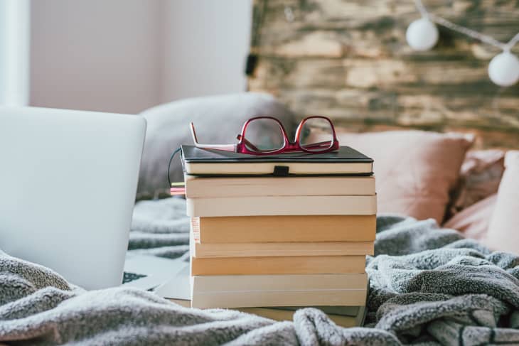 pile of books with glasses and a laptop on the bed at home