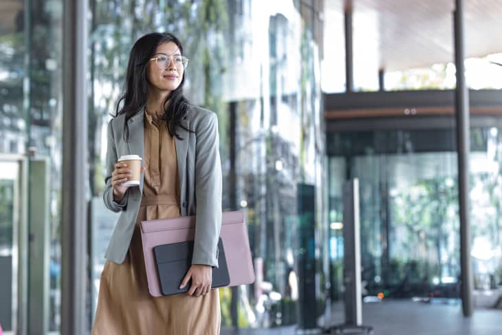 Outdoor shot of a smiling Asian businesswoman holding coffee and files on the street.