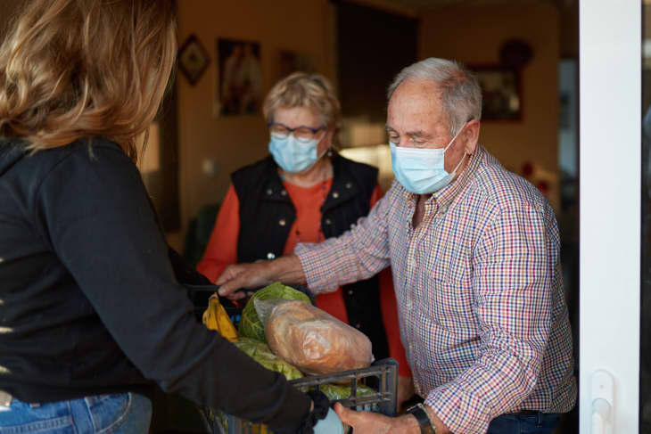 Young woman delivering groceries to an elderly couple wearing face masks
