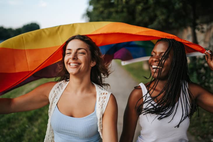 年轻的多民族女同性恋夫妇举着彩虹旗在城市码头上奔跑
