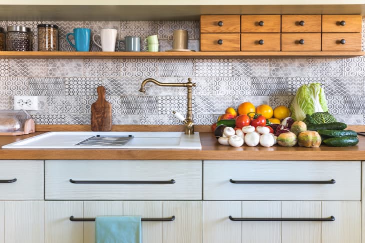 Stack of edible mushrooms, vegetables and fruits (tomatos, avocado, zucchini, oranges, apples, grapefruits, kohlrabi, chinese cabbage, savoy cabbage, cucumbers, radicchio) on countertop in modern rustic kitchen.