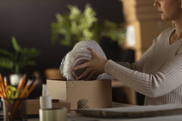 Cut out shot of young female entrepreneur packing customer's order wrapped in a bubble wrap in a cardboard box and getting it ready for shipping.