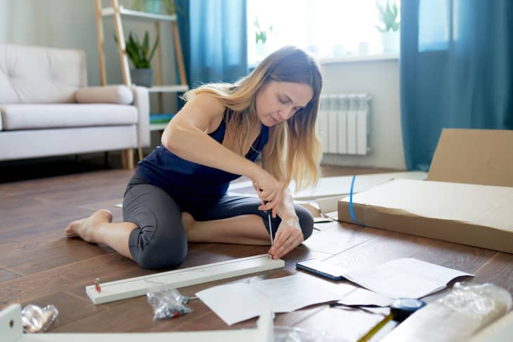 A young woman with the help of instructions makes the assembly of a new table with drawers in her apartment. Furniture assembly. Relocation and renovation.
