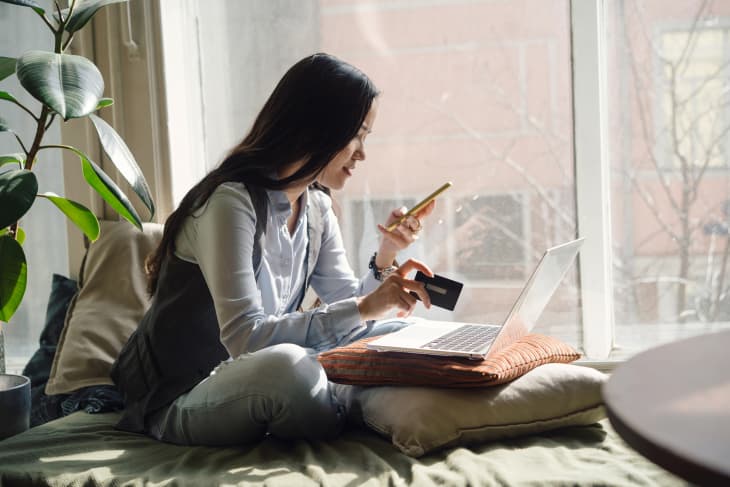 Woman in blue jeans sitting on the bed in a yoga pose in front of a laptop