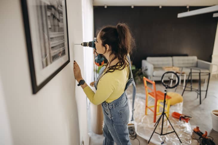 Woman drills a wall in her new apartment she is renovating