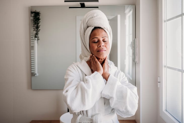 Smiling mature woman massaging face in bathroom at home