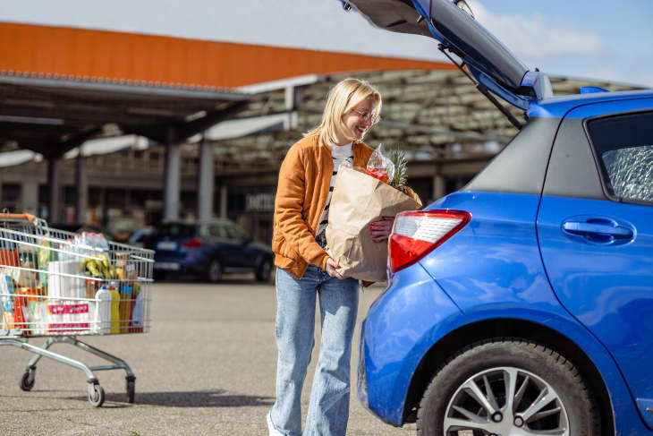 Young woman smiling while putting groceries in the trunk of her car
