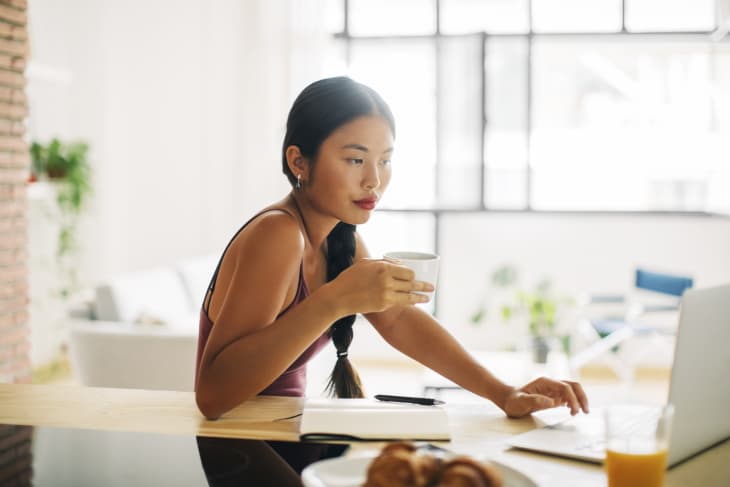 Woman with cup of coffee working with laptop at home
