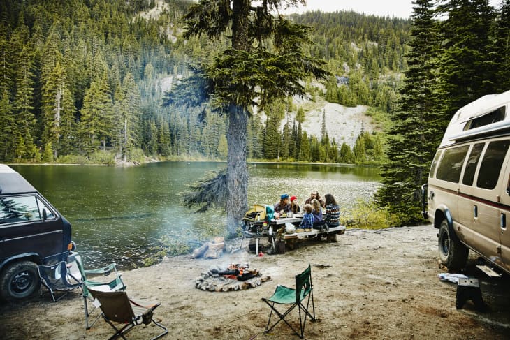 Friends sharing a meal while camping by lake.