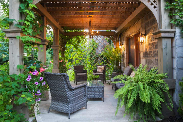 Rear of Renaissance grey stone and mortar castle style home with concrete patio and lattice covered wooden gazebo