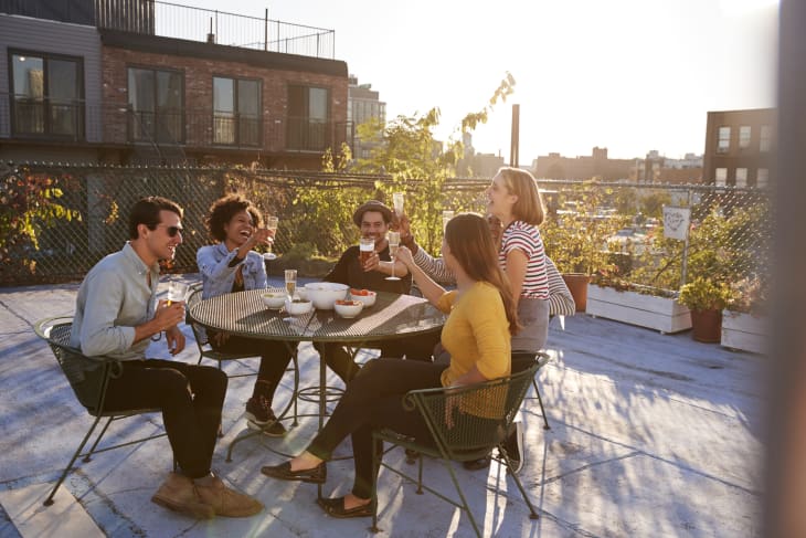 Five friends sitting at a table on a rooftop making a toast