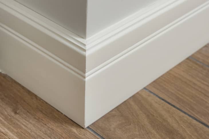 Molding in the interior, baseboard corner. Light matte wall with tiles immitating hardwood flooring.