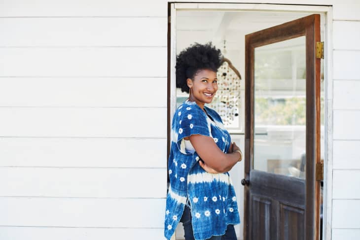 Person in a blue tie-dye shirt standing in a doorway, smiling with arms crossed.