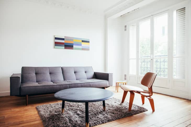 Modern living room with a gray sofa, round coffee table, wooden chair, and abstract wall art.