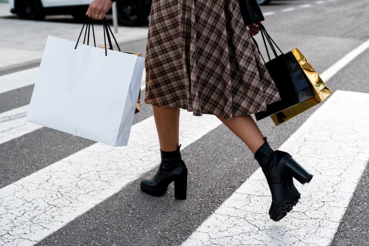 woman walking through a crosswalk carrying paper shopping bags