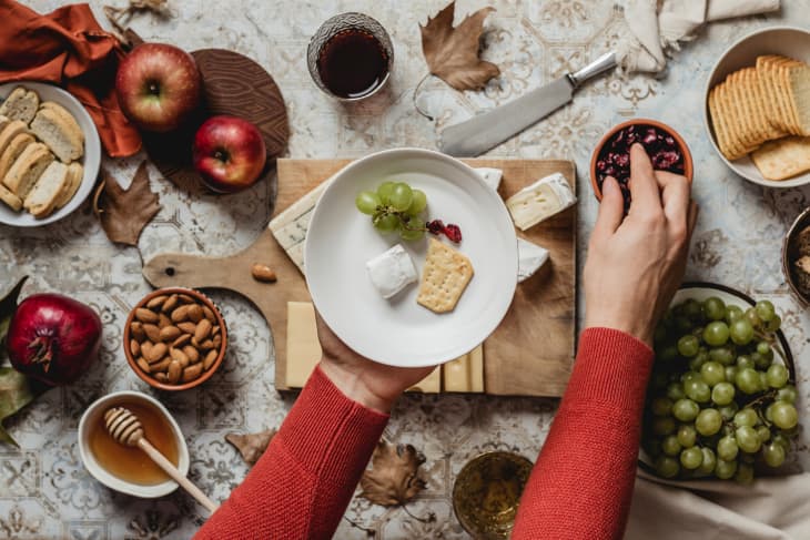 Handing reach out with a plate to a Table With Cheese, Fruits, Crackers And Wine