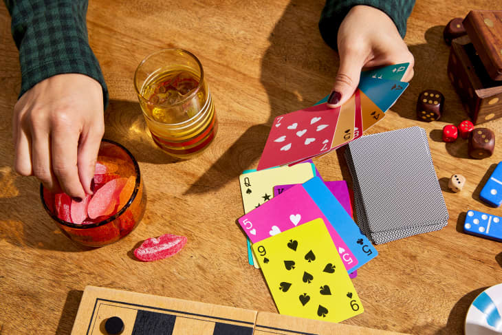 Hands of someone playing cards at table. The cards are bright and colorful. Snacks and other games on table