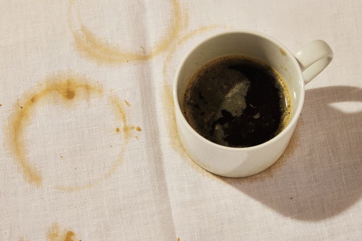 Cup of coffee on off-white tablecloth. There are ring shaped coffee stains on the tablecloth fabric