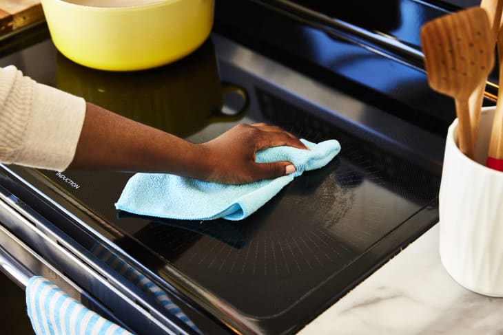 Someone cleaning a black glass stovetop with a blue microcloth