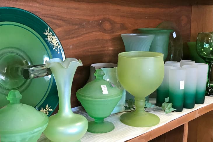 Shelves of used green glassware dishes for sale on shelf in thrift shop store